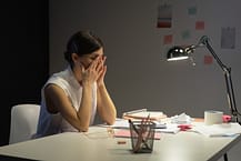 woman sitting at her desk with her hands on her face overworking